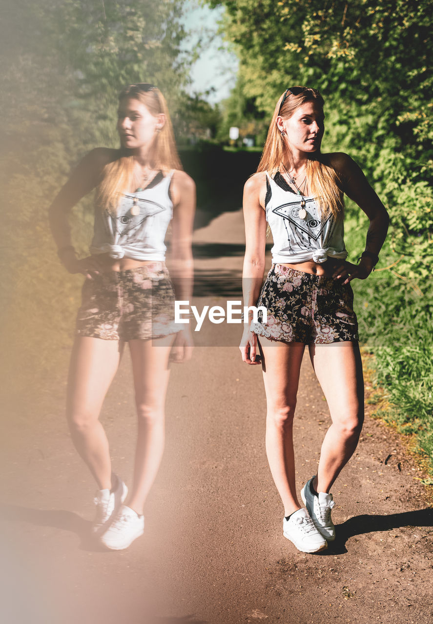 Digital composite image of young woman reflecting in glass while posing on footpath