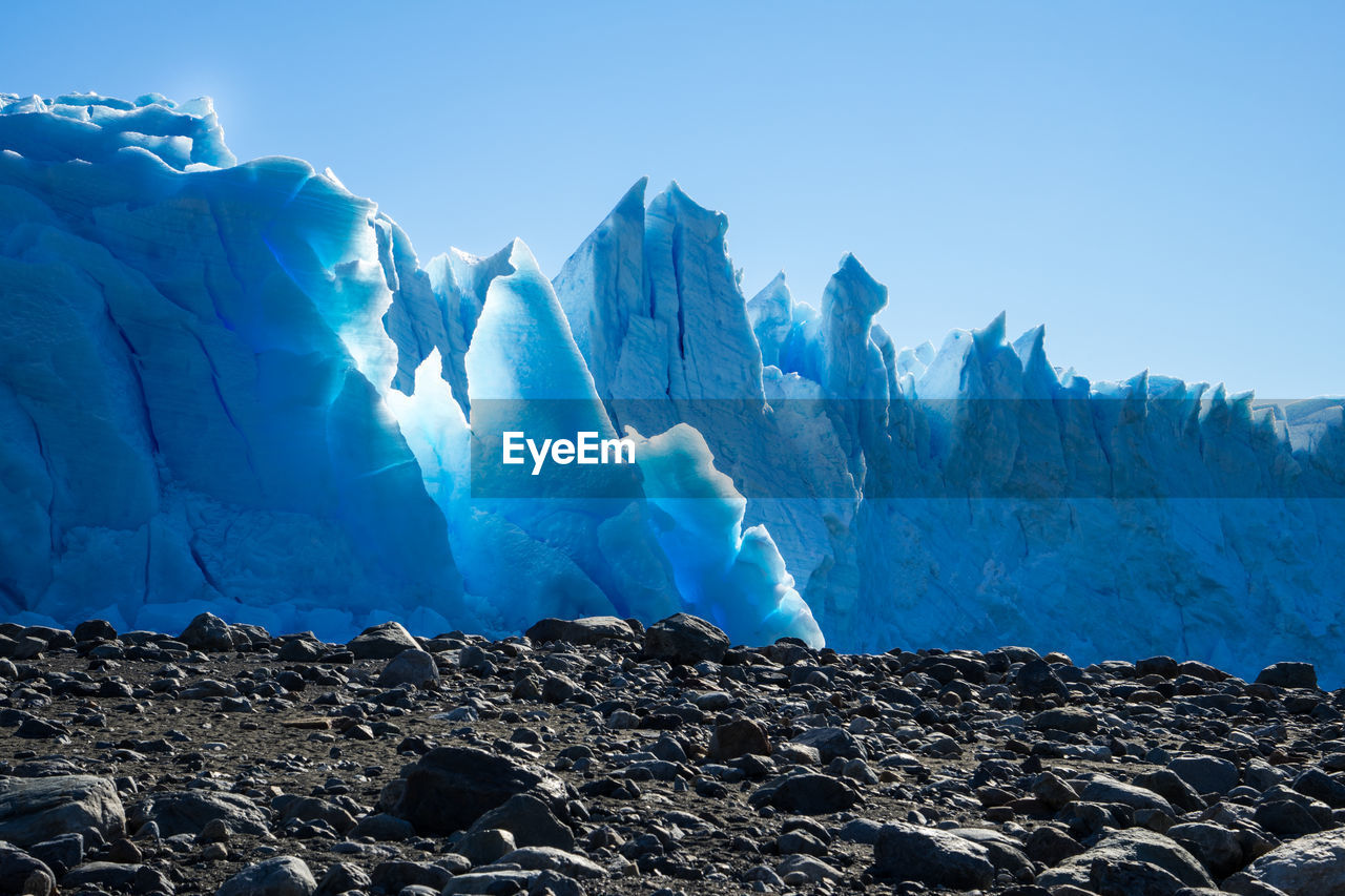 Scenic view of glaciers by rocks against clear blue sky