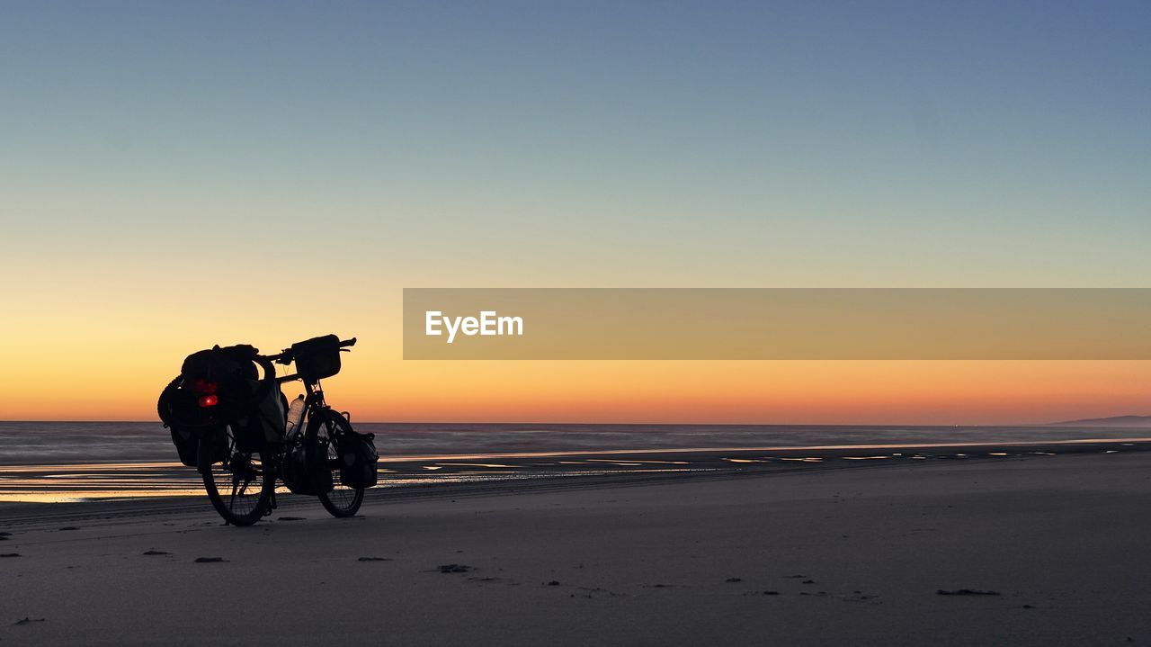 Motorcycle on beach against clear sky during sunset