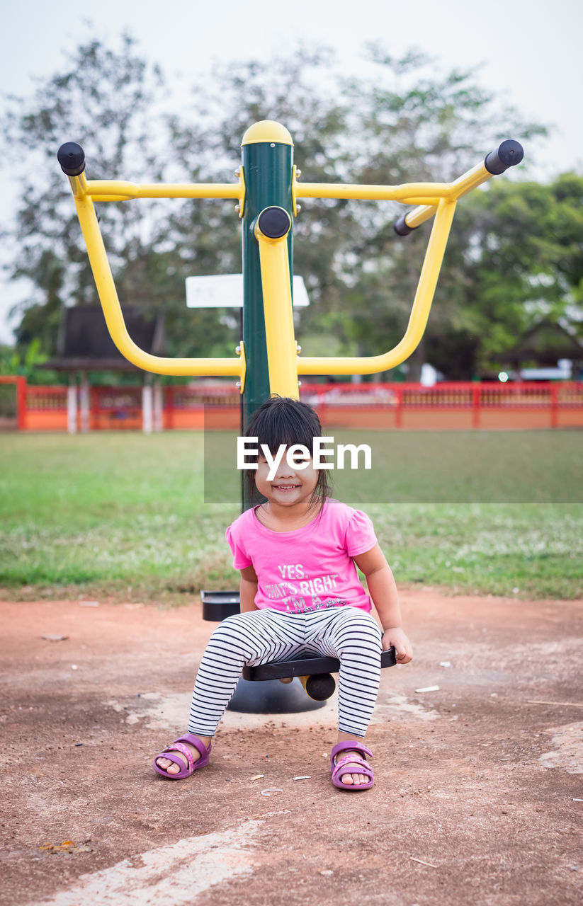Full length portrait of cute girl sitting on exercise machine in park