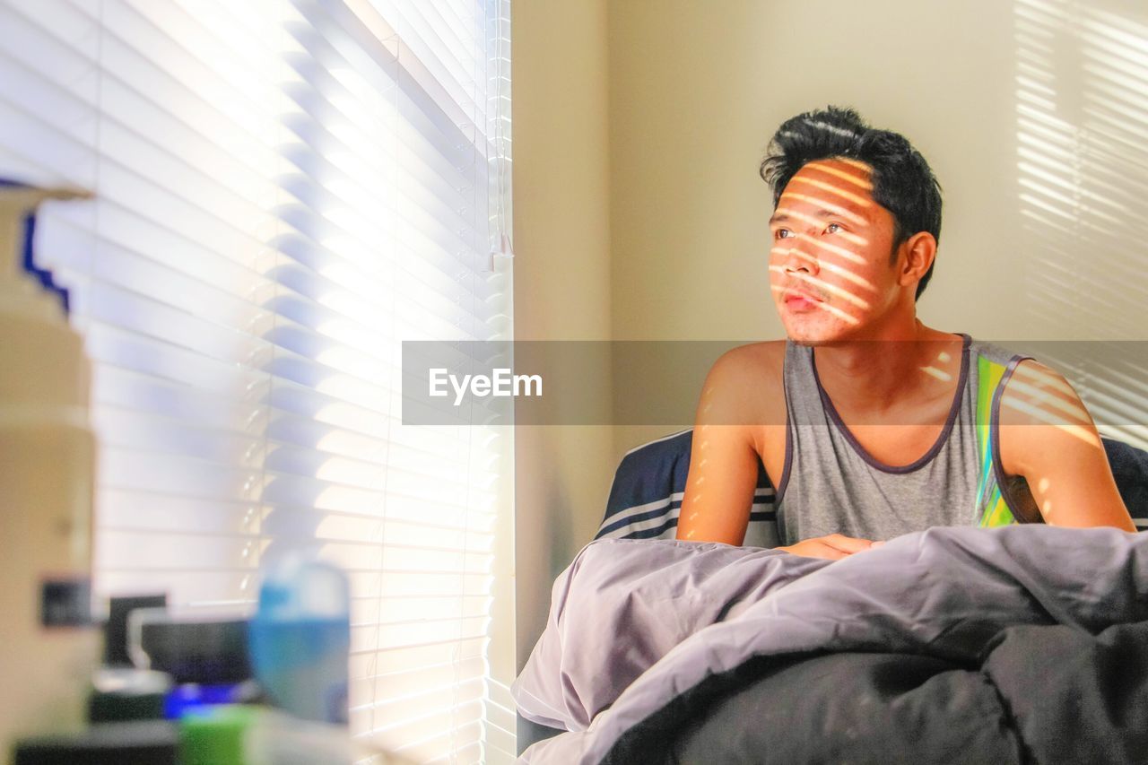 Man looking away on bed in sunny day