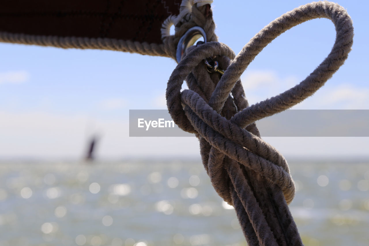 Close-up of rope tied on metal against sky
