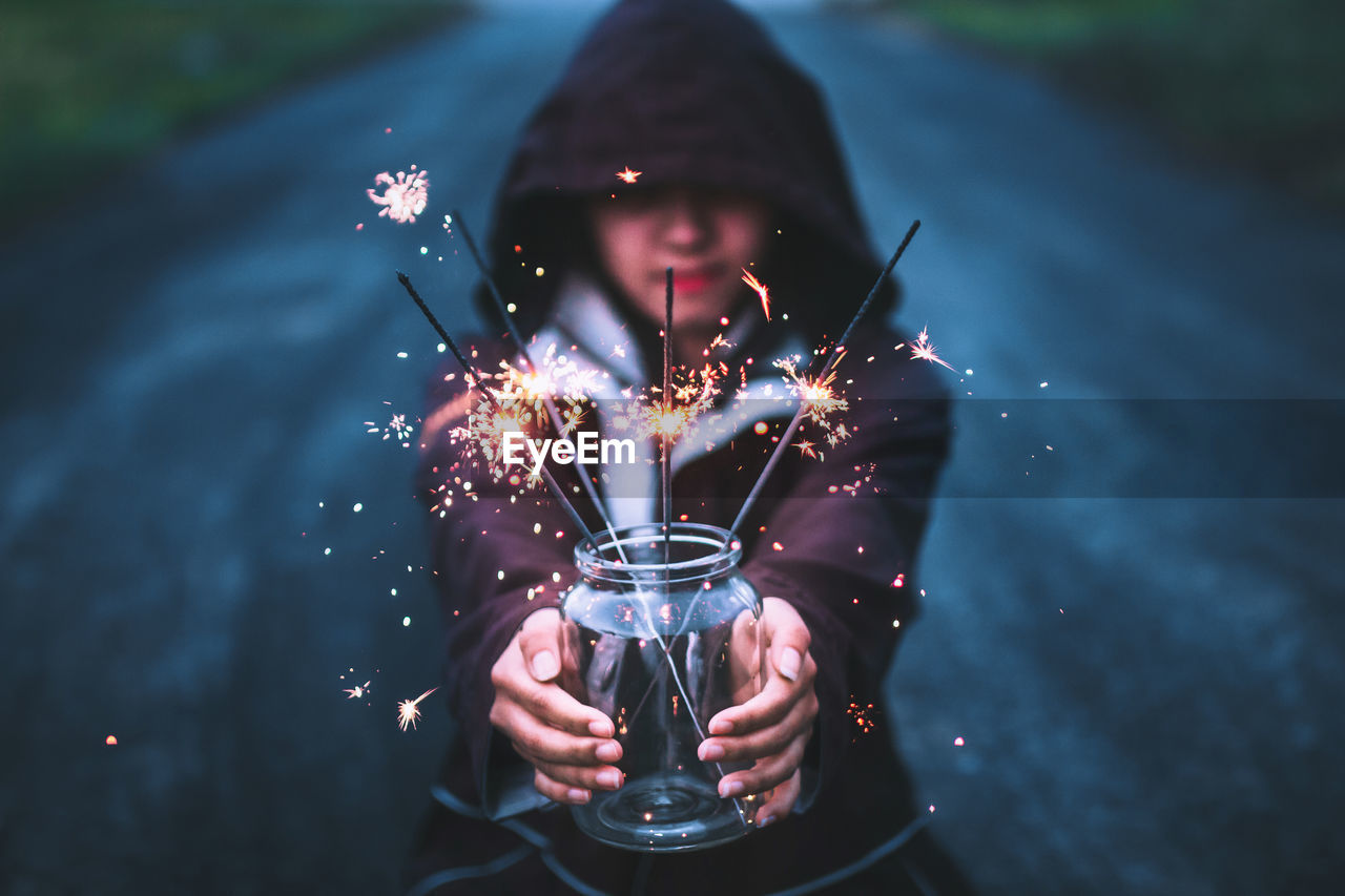 Young woman holding sparklers in jar on road