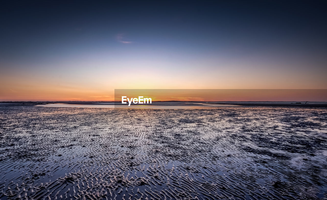 Tranquil view of mud flat against clear sky during sunset