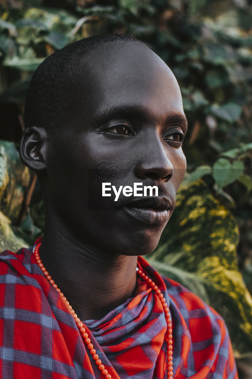 Maasai man in traditional clothes standing in front of green leaves