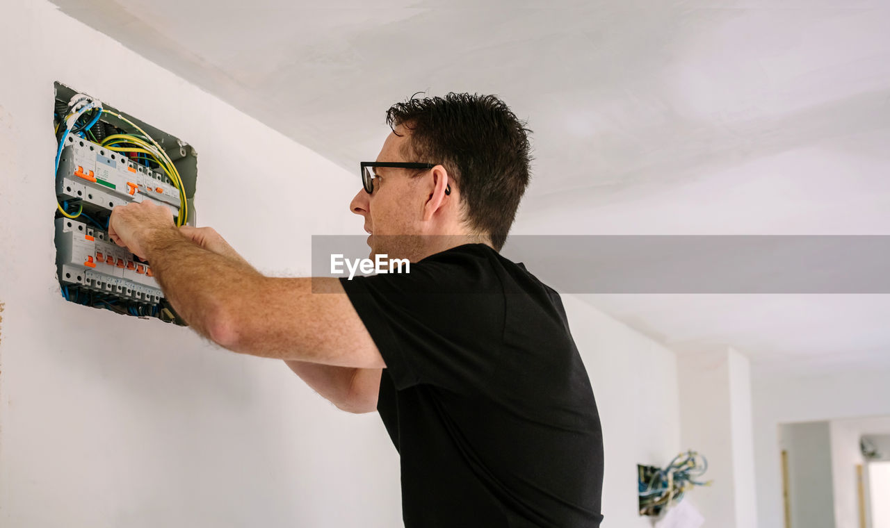 Side view of man standing against wall at home