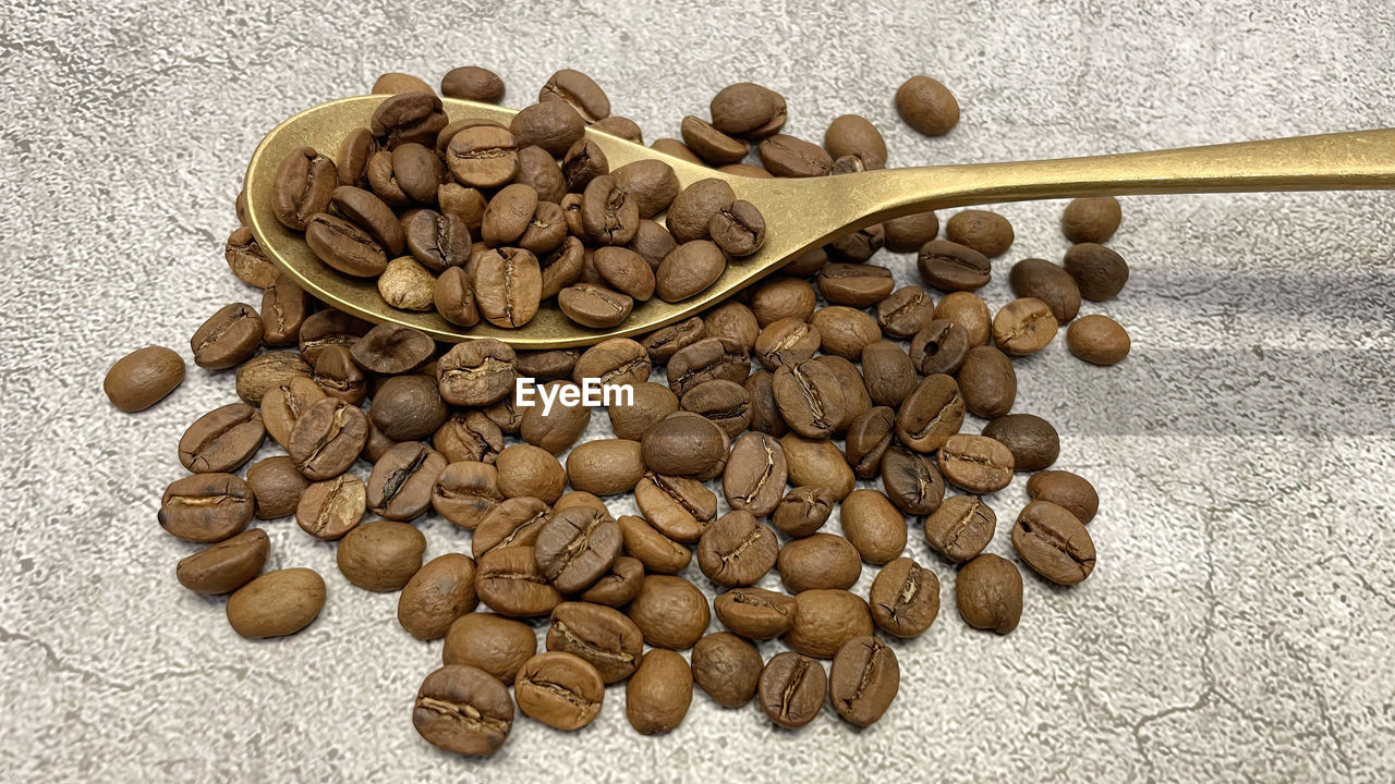 Close up roasted coffee beans in metal spoon on gray background