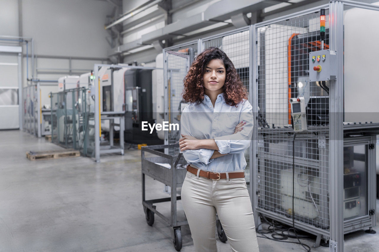 Smiling engineer with arms crossed standing in front of machine