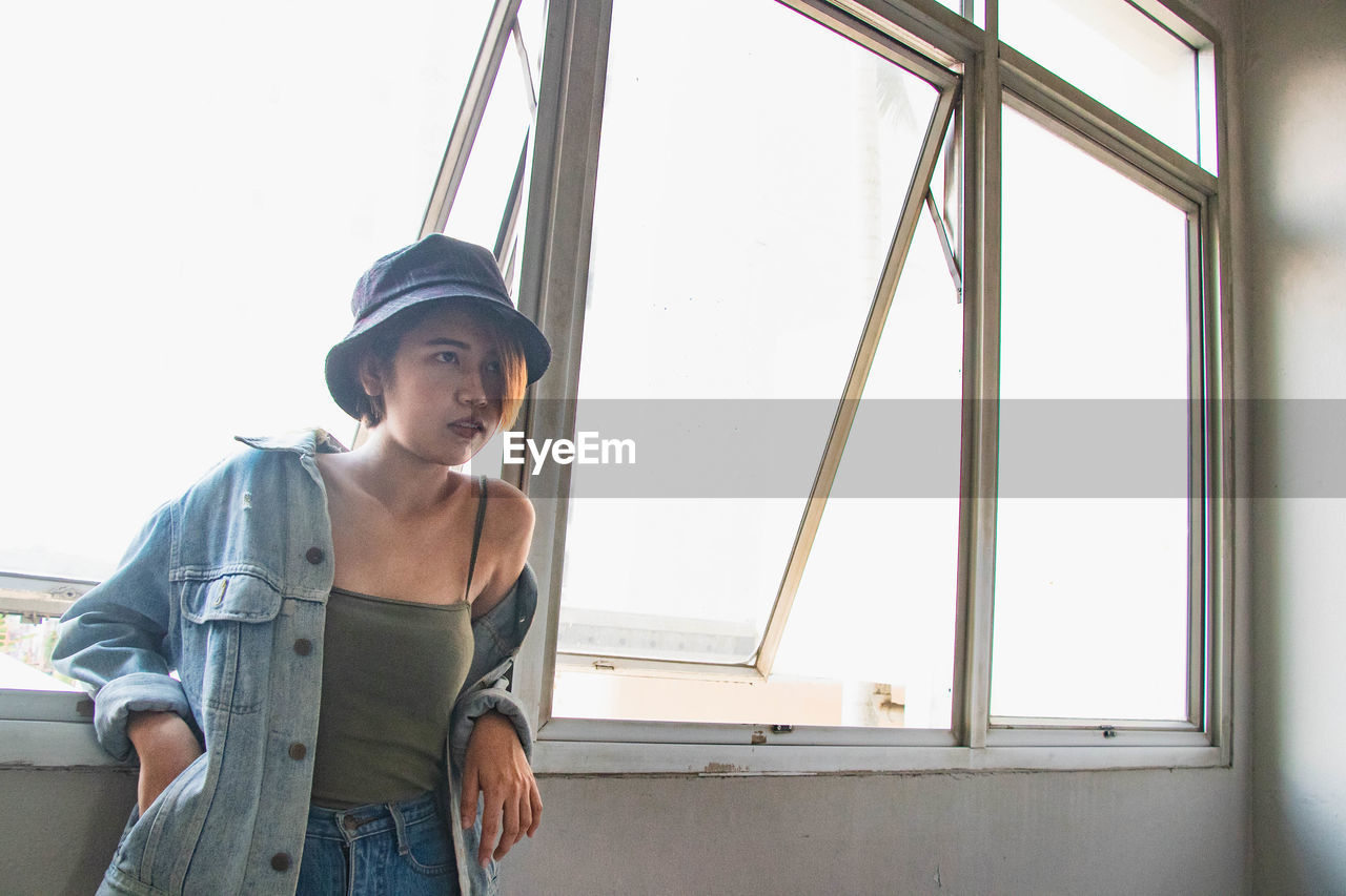 Young woman looking away while standing by window