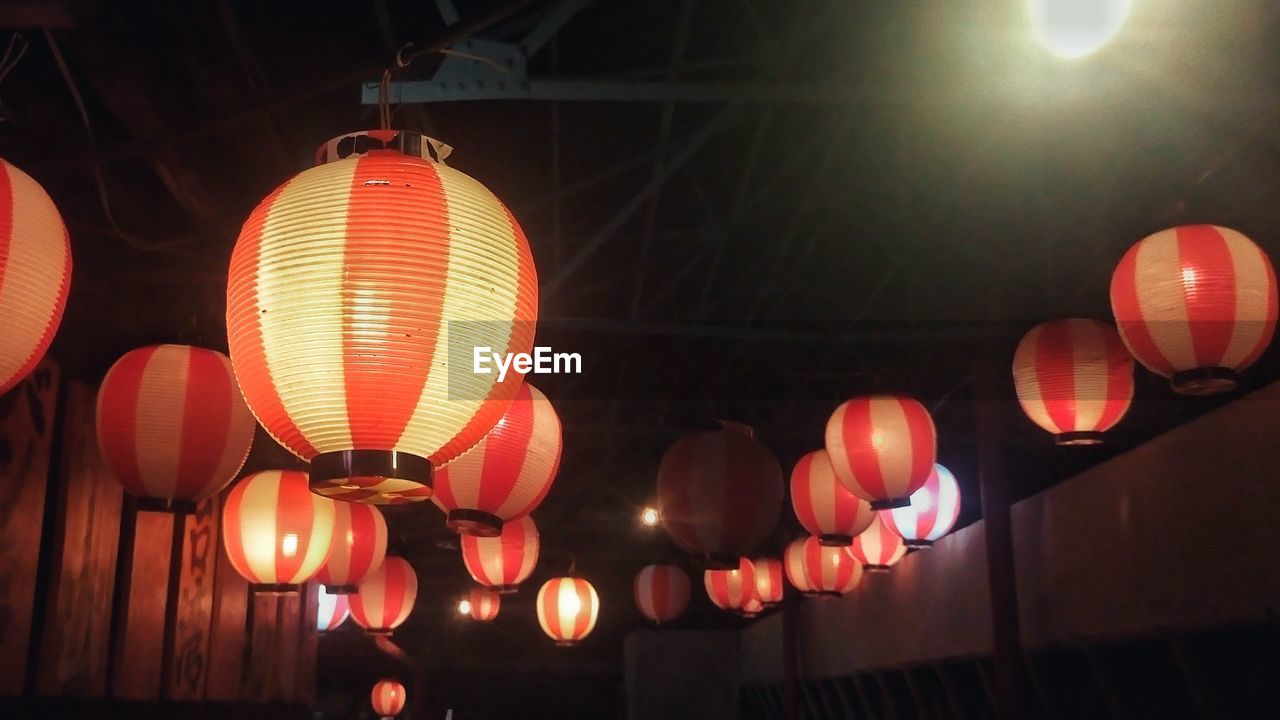 LOW ANGLE VIEW OF ILLUMINATED LANTERNS HANGING IN ROW