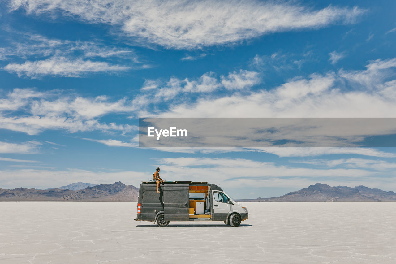 Young man sitting on roof of camper van in bonneville salt flats.