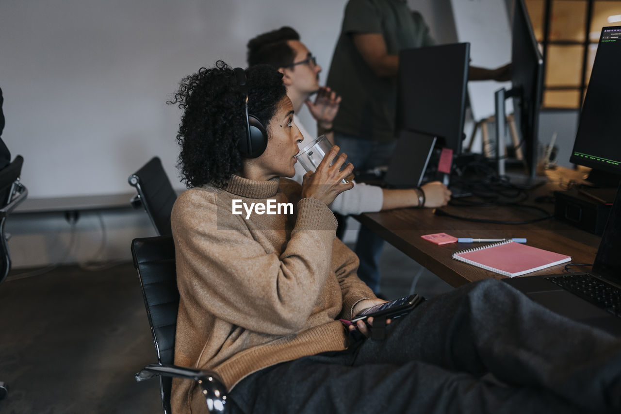 Businesswoman drinking coffee while looking at computer hacker working in startup company