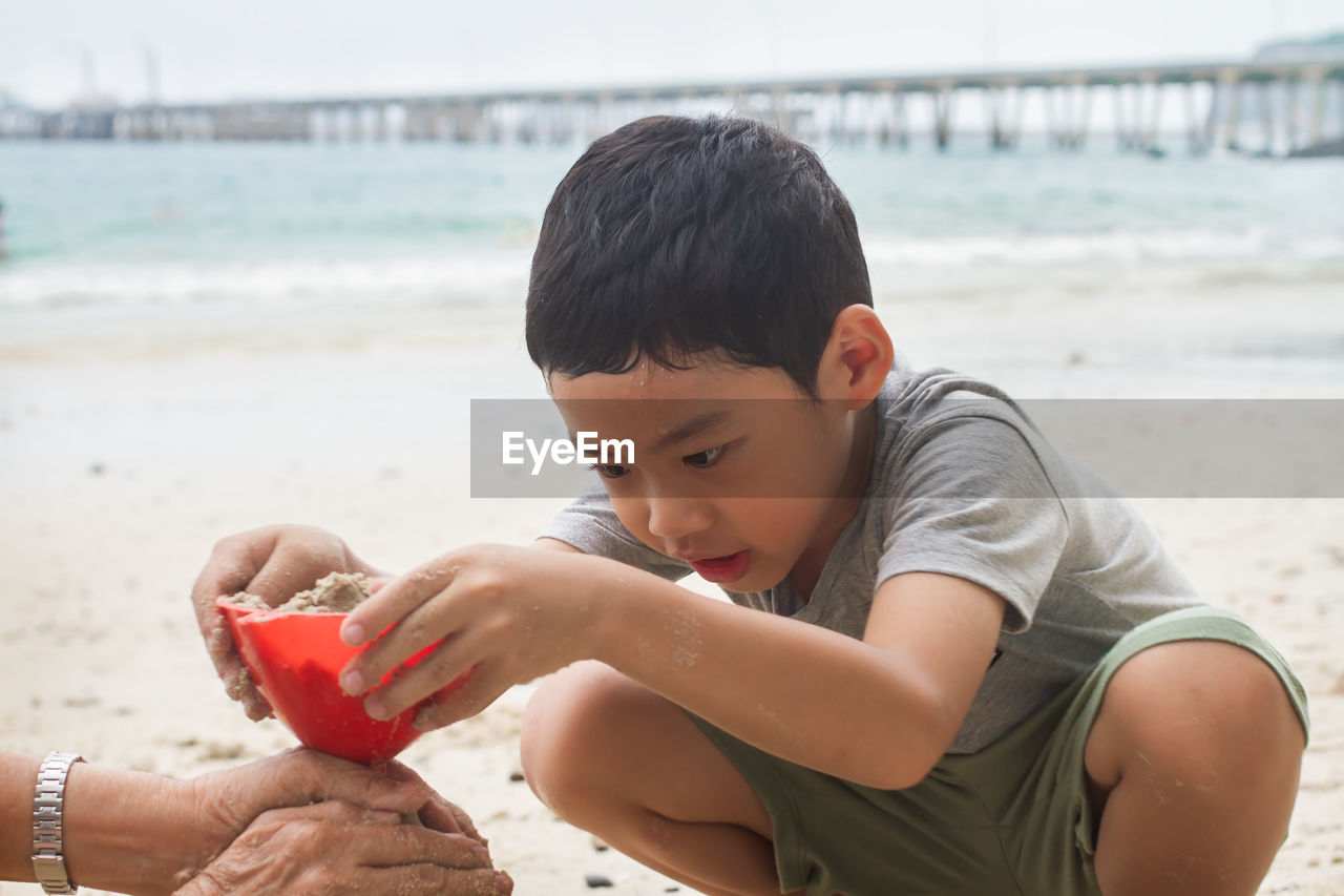 Cropped hands of granddaughter and son making sandcastle at beach