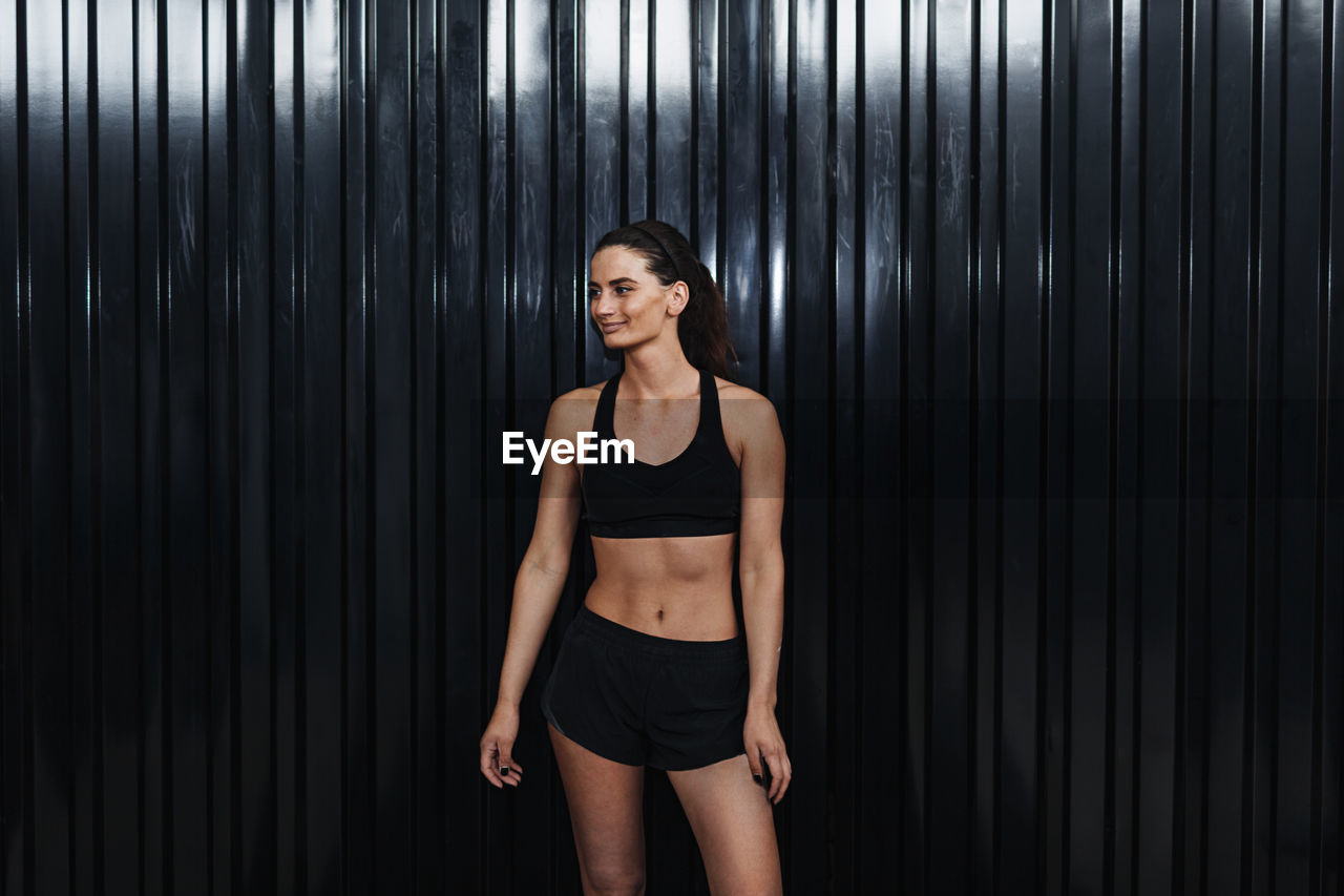 Young female athlete in sports clothing standing by corrugated iron