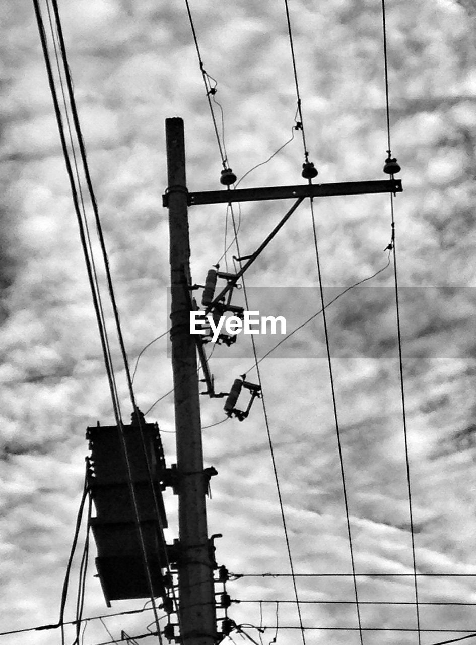 Low angle view of electricity pylon against cloudy sky