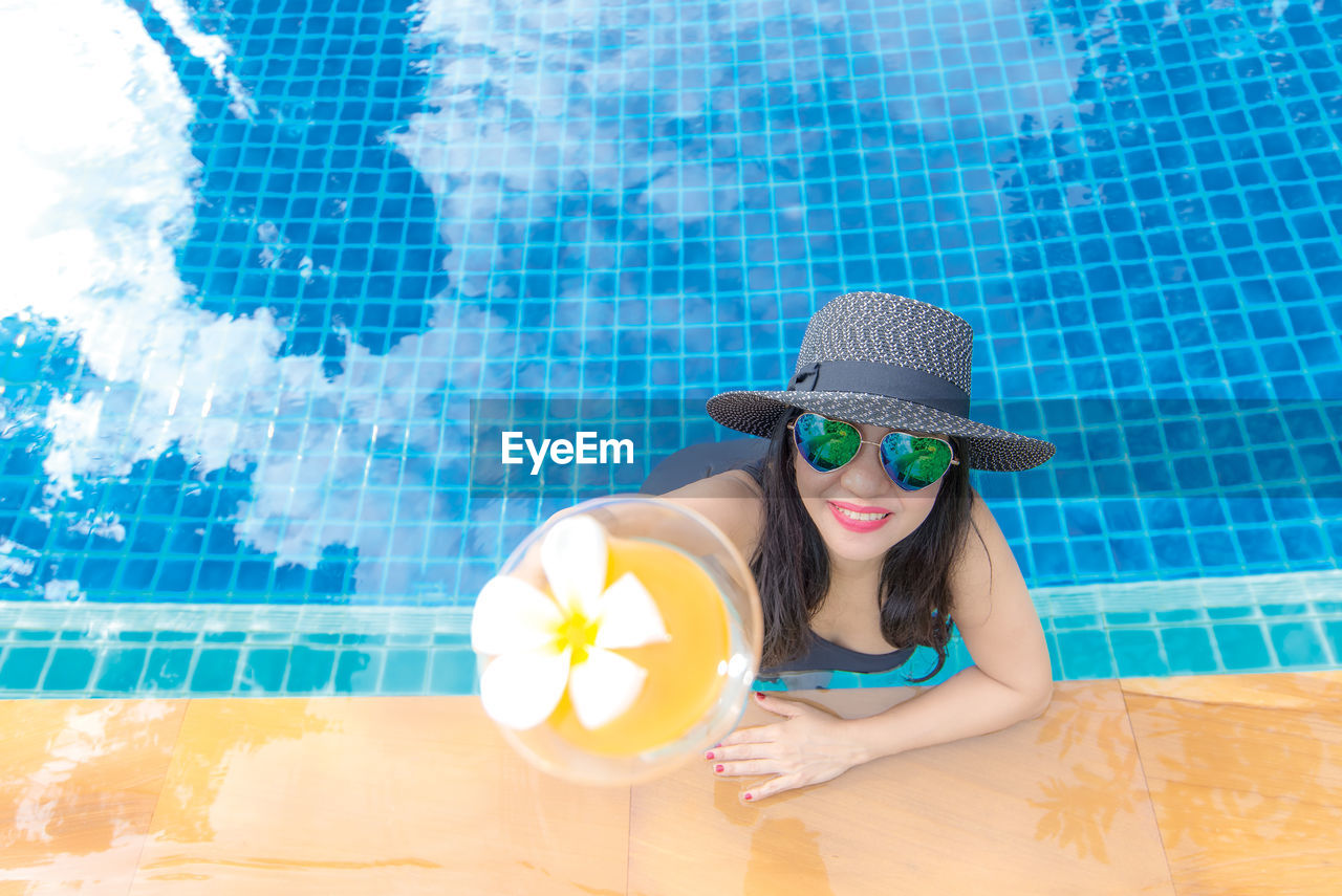 PORTRAIT OF YOUNG WOMAN WEARING SUNGLASSES IN SWIMMING POOL AGAINST WALL