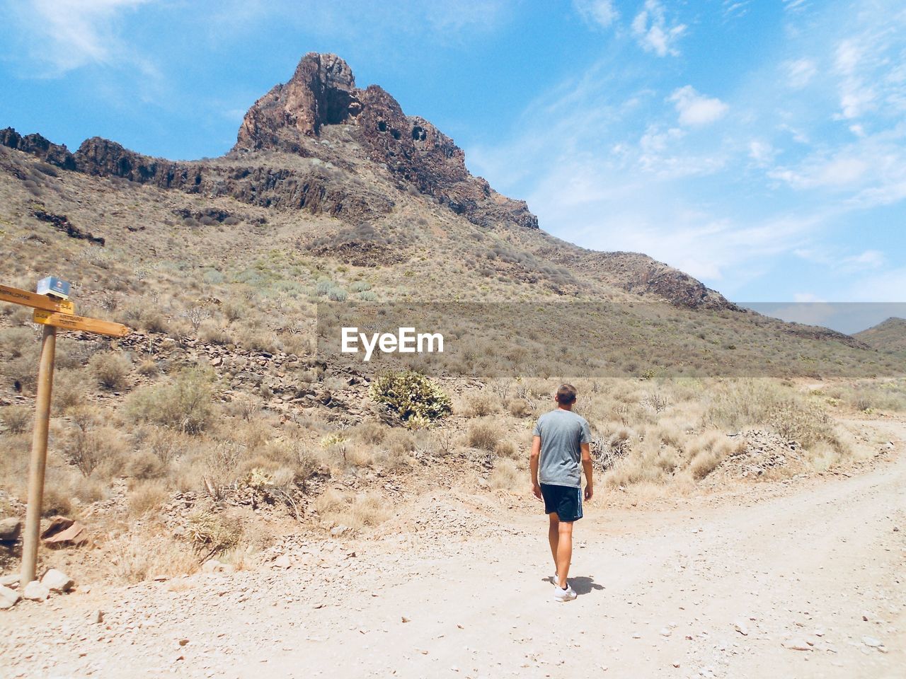 Rear view of man walking on dirt road against mountains