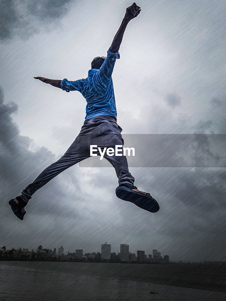 Low angle view of excited man jumping in mid-air against sky during rain