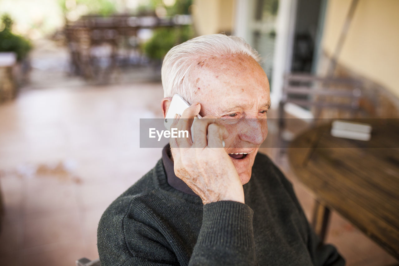 Elderly man talking on the phone on the porch of his house