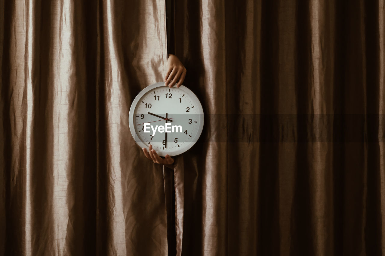 Close-up of hand holding clock on curtain