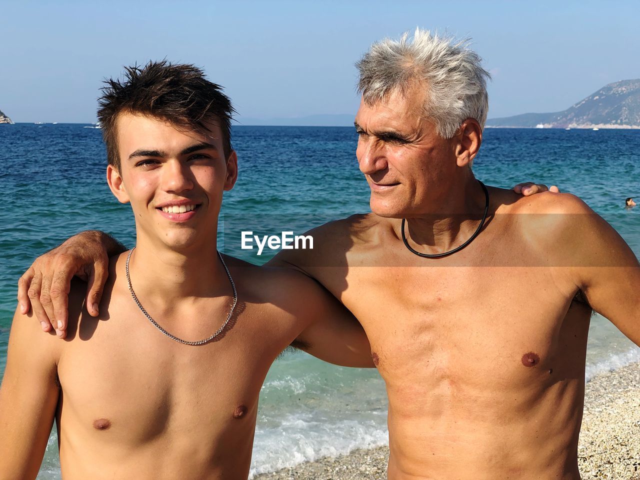 Smiling father and son at beach against sky