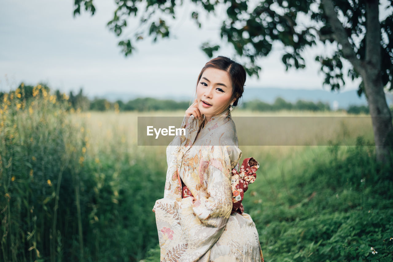 Portrait of young woman wearing kimono standing on field