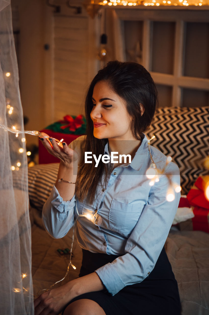 Smiling young woman with illuminated string light at home