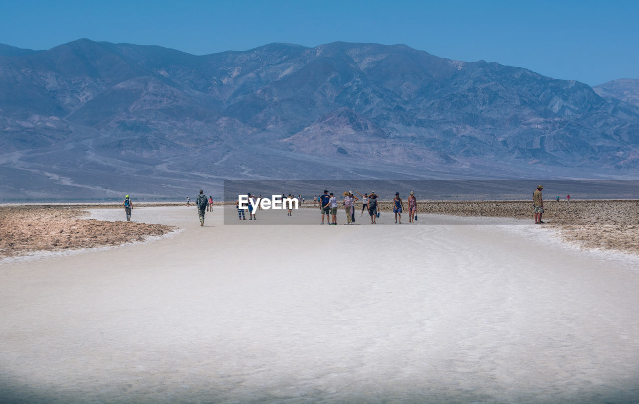 People walking on sand dune by mountain against clear sky