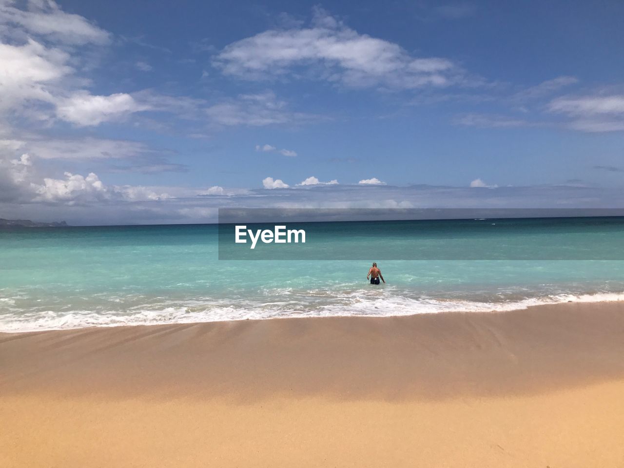 Rear view of shirtless man in sea against cloudy sky during sunny day