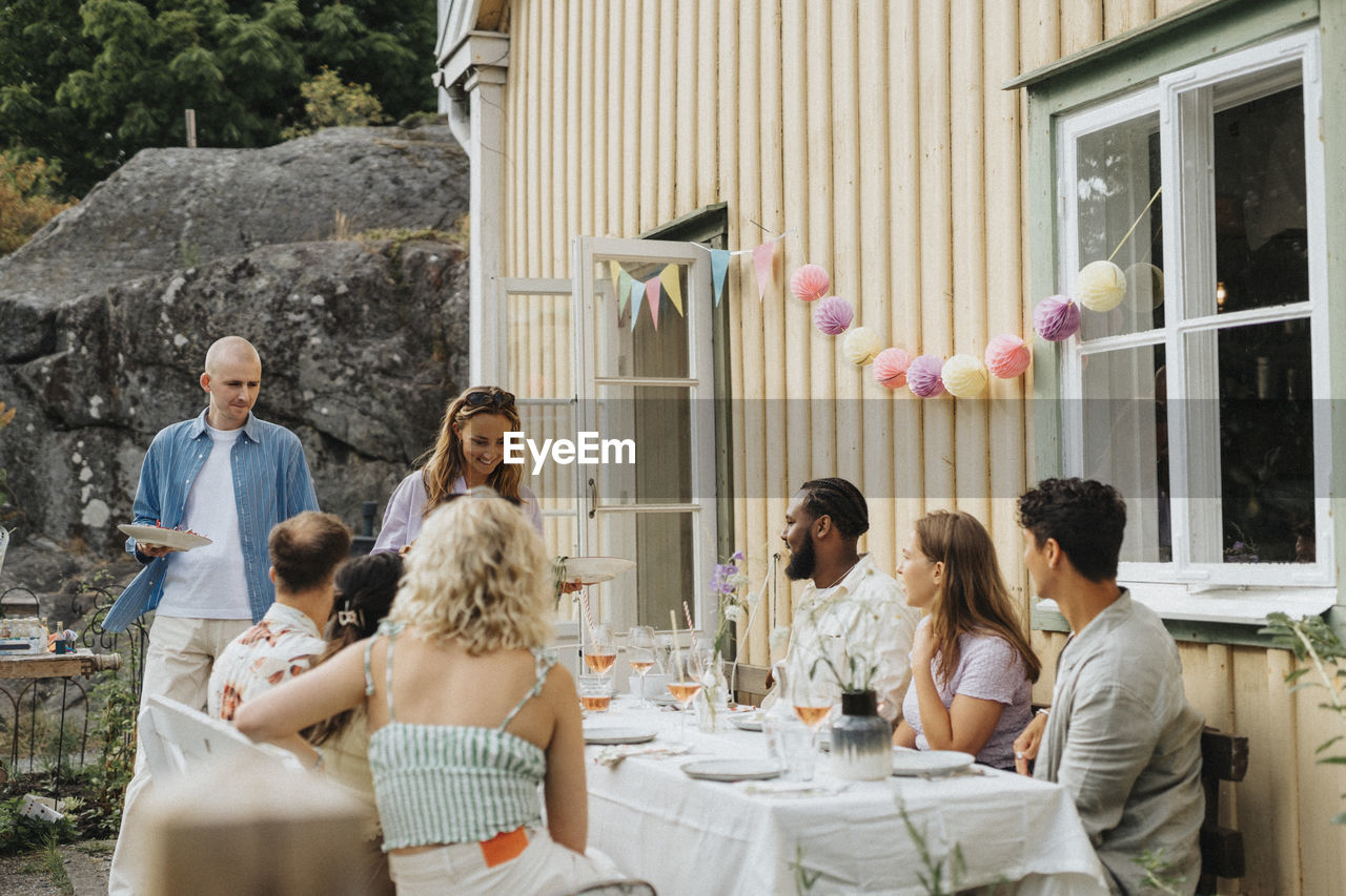 Smiling woman serving food to male and female friends during dinner party at cafe