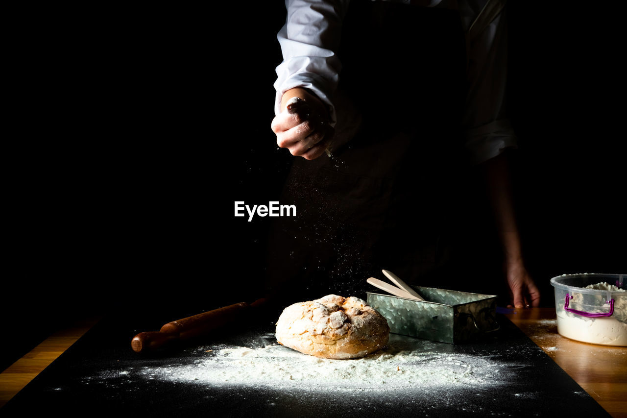 Rye bread and female chef hands with falling flour on black background. close-up