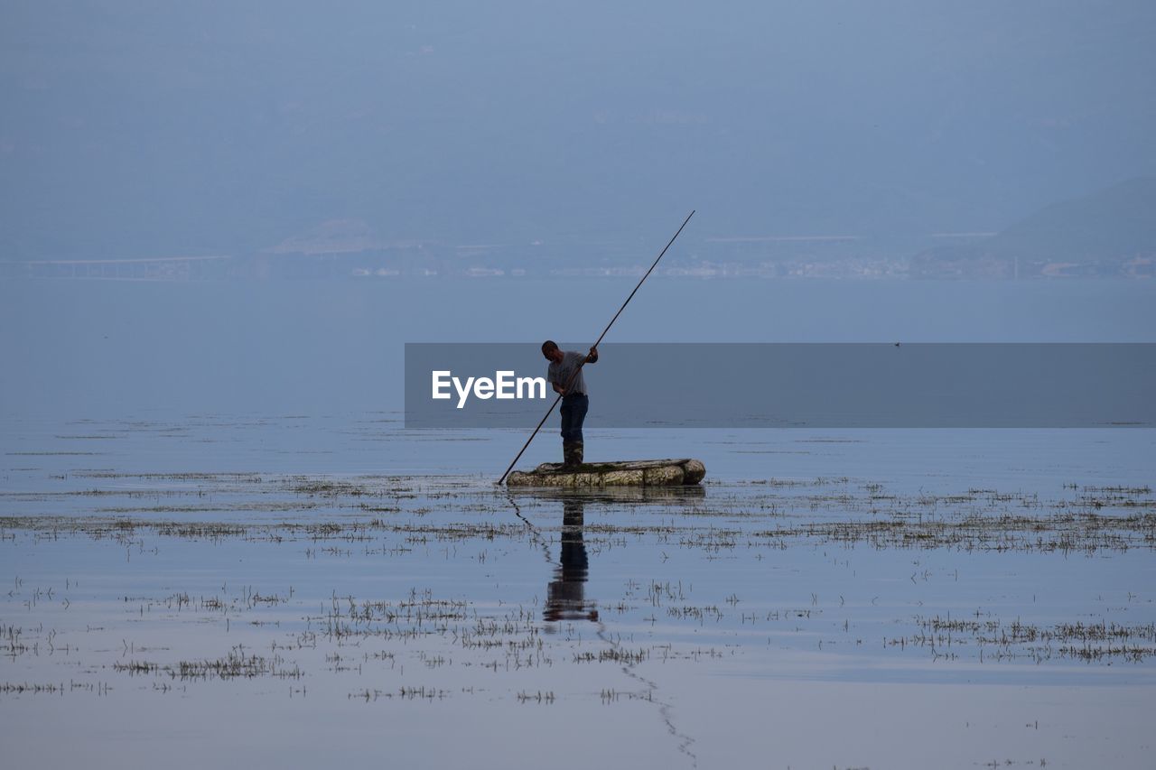 Man fishing in lake against sky