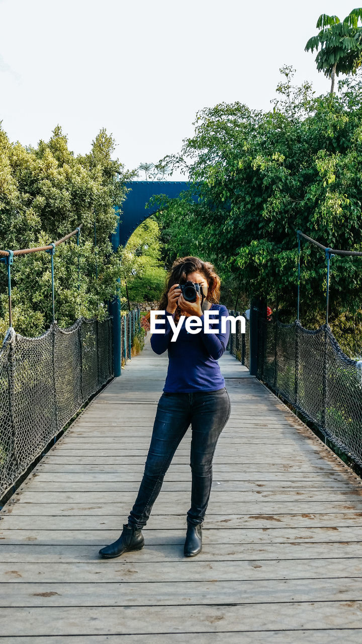 Full length of woman photographing on footbridge