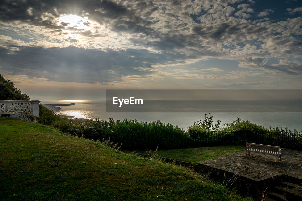 Empty bench by sea against sky