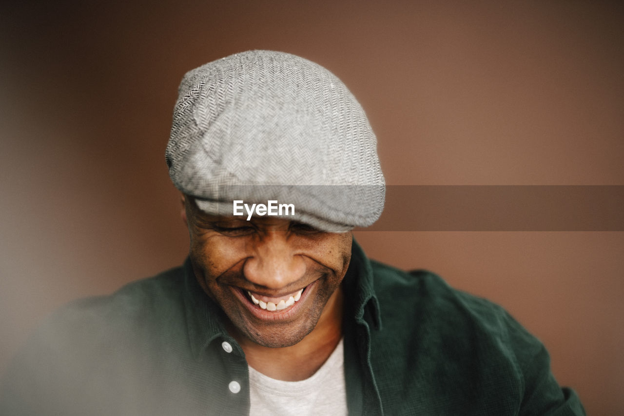 Happy mature man wearing beret looking down over brown background