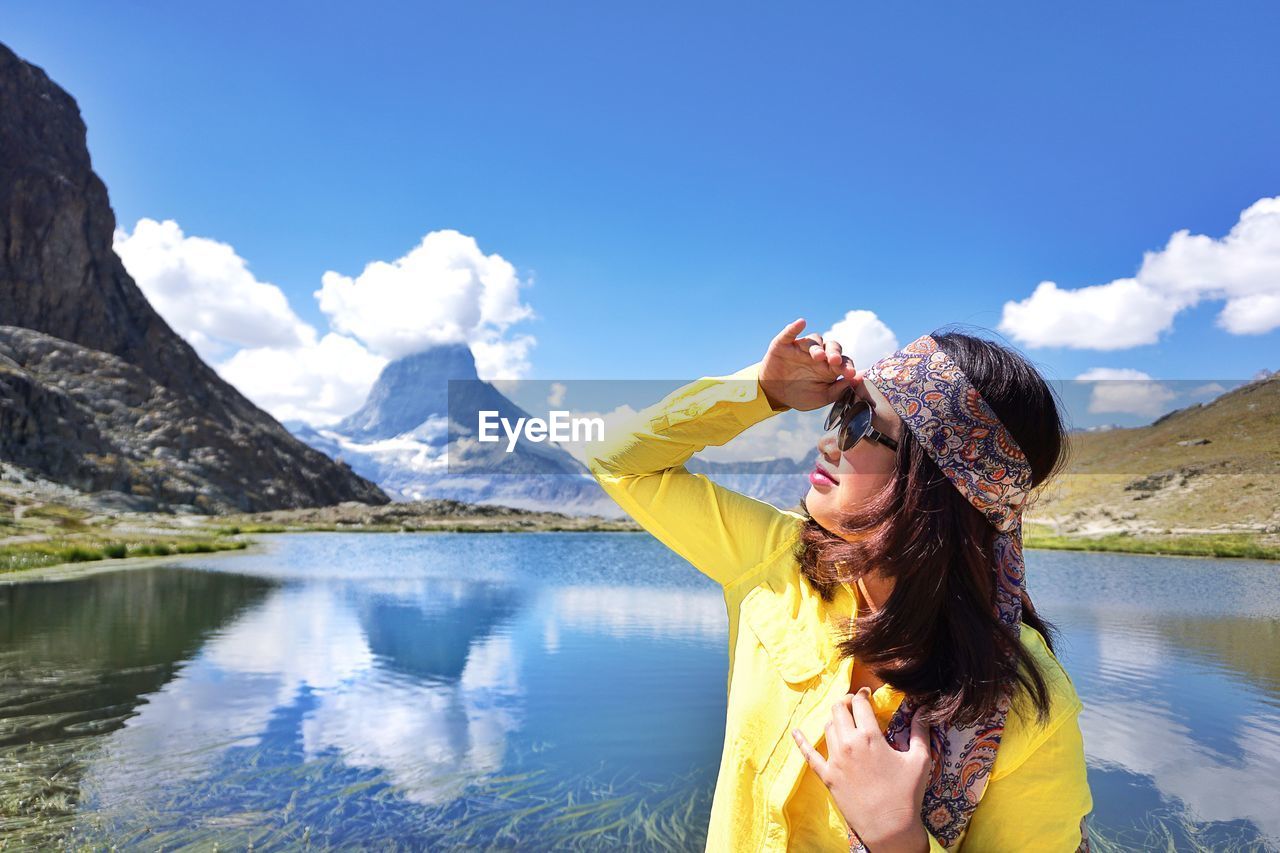 Woman shielding eyes while standing against lake and mountains