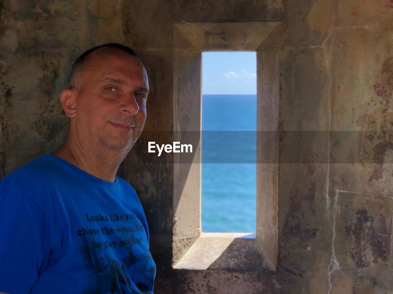 Portrait of smiling man standing by window against sea