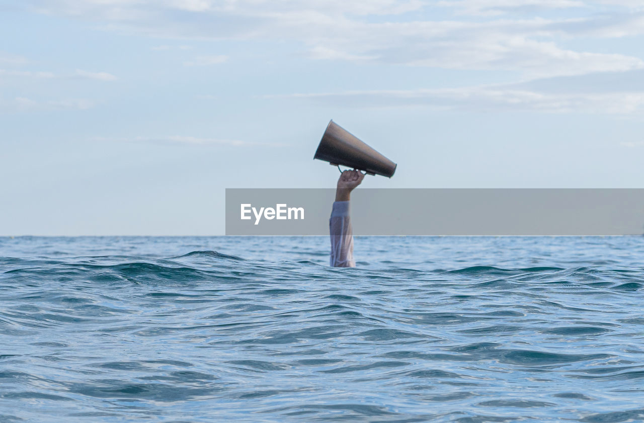 Cropped image of a hand with a megaphone into the  sea against sky