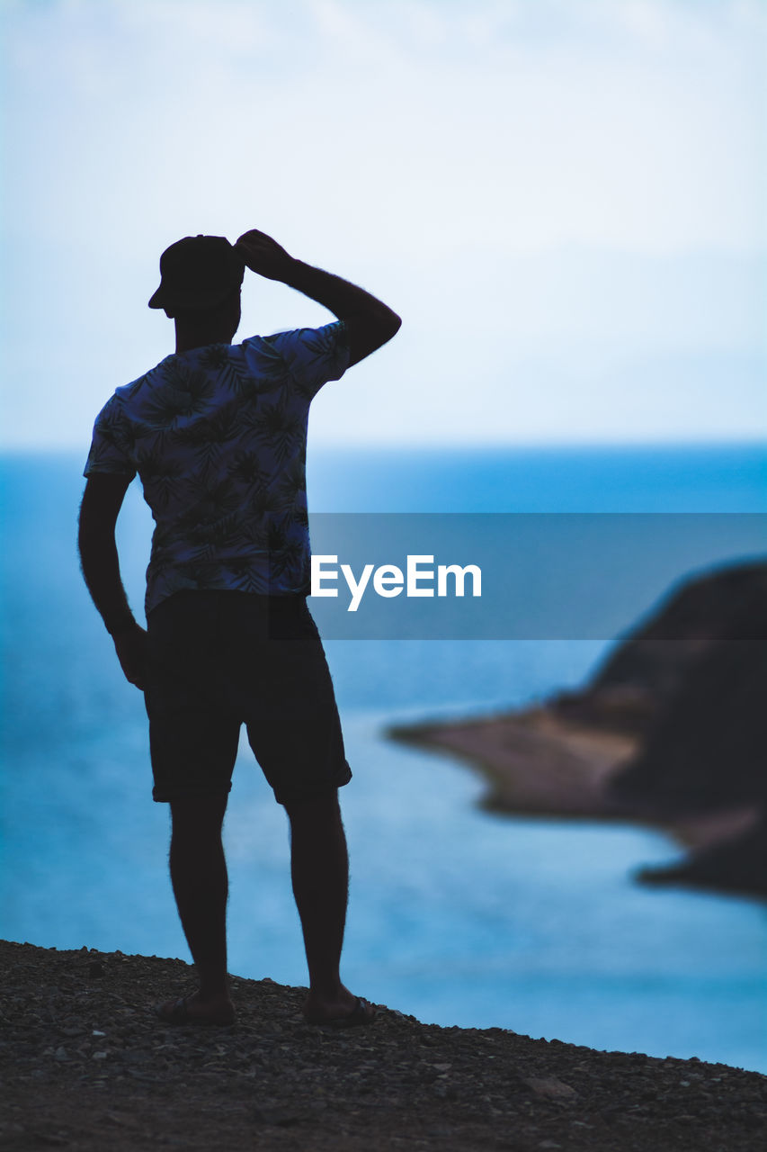 Rear view of man standing on rock by sea against sky