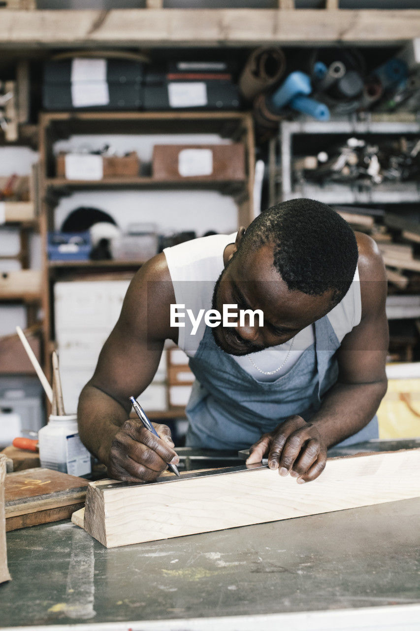 Male entrepreneur marking on wood while upcycling at workshop