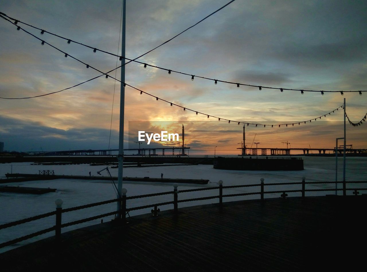 Promenade by harbor against sky during sunset