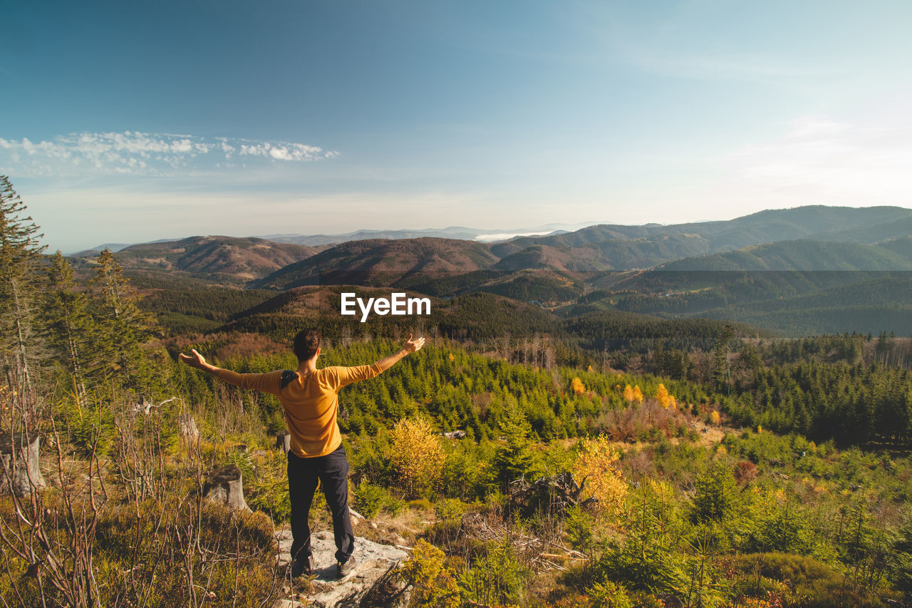 Enthusiastic traveller stands on rock and looks down into the valley. happy to have reached his goal