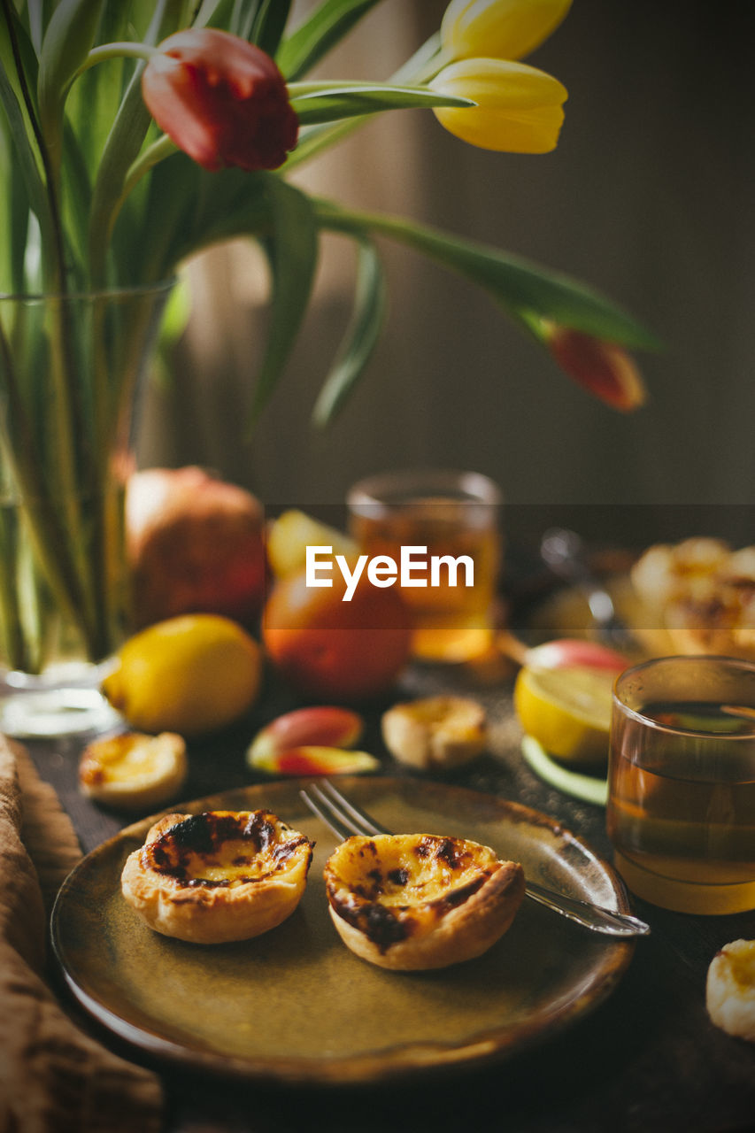 Pastel de nata and tea on table with fruit and tulip in background