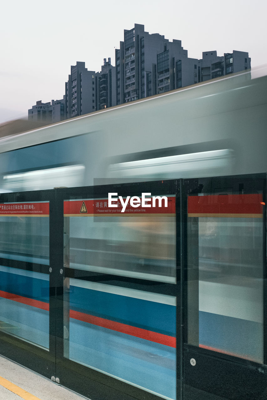 architecture, transportation, transport, city, public transportation, mode of transportation, public transport, rail transportation, train, speed, motion, built structure, blurred motion, building exterior, vehicle, travel, railroad station, sky, subway train, city life, no people, on the move, railroad station platform, station, outdoors, building, subway