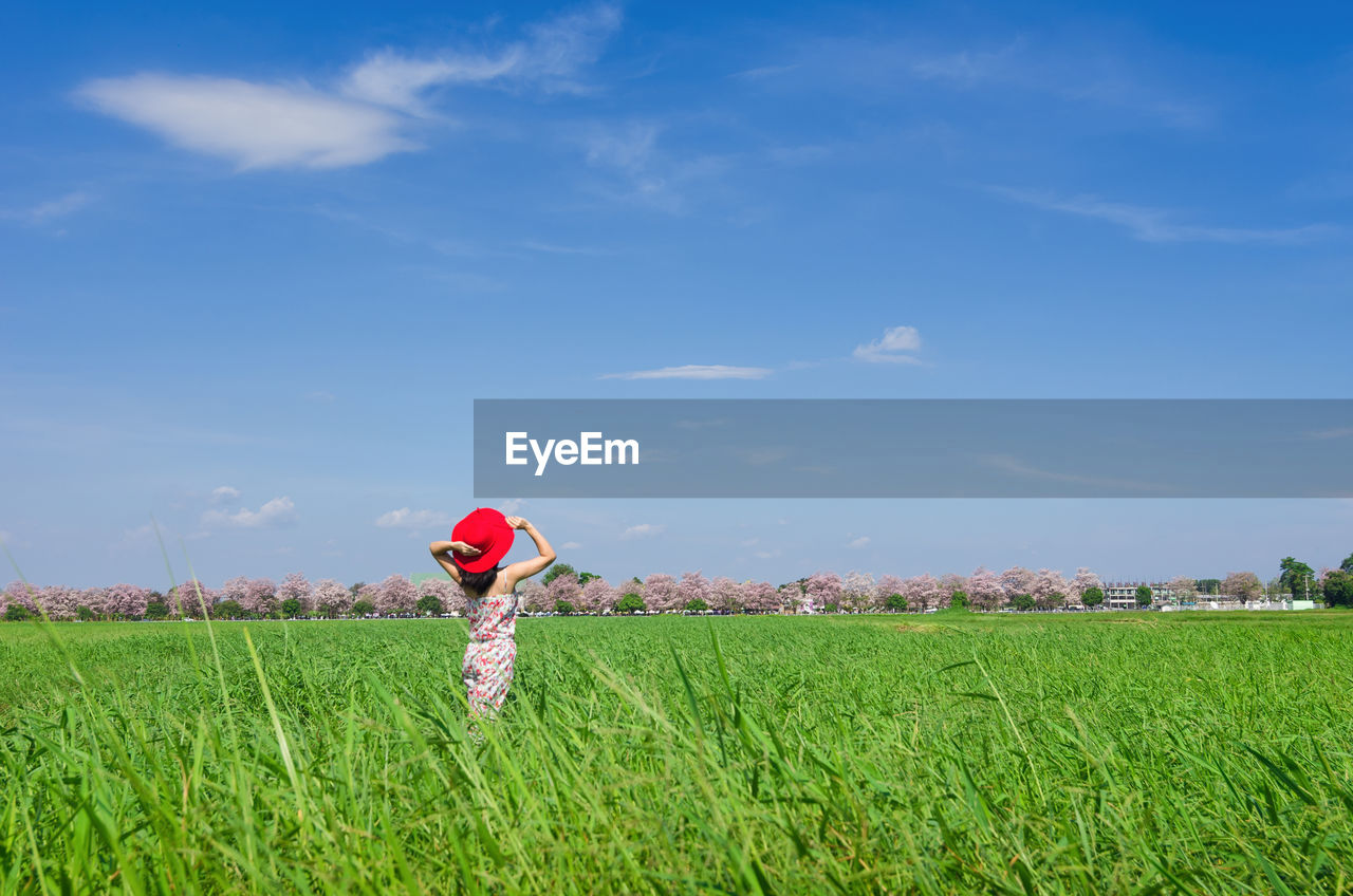 Woman standing amidst plants on field against sky during sunny day