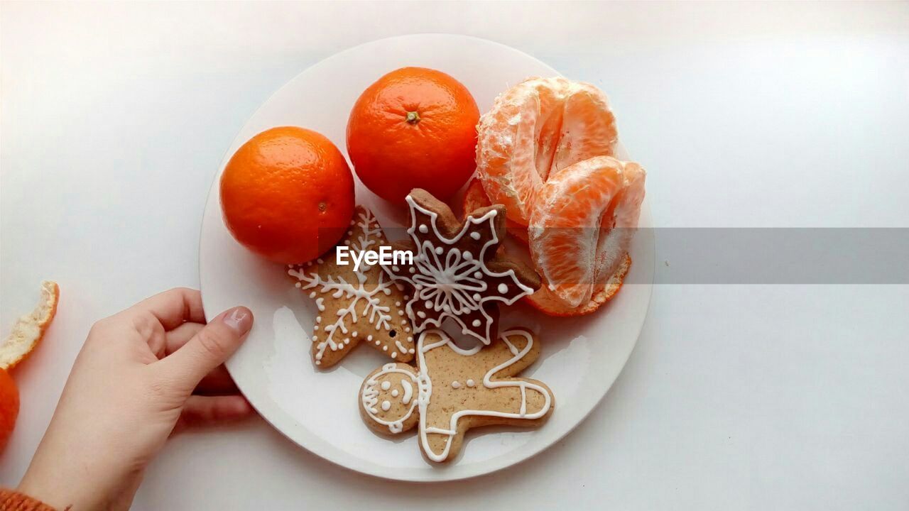 Close-up of woman hand holding orange fruit, cookies. christmas