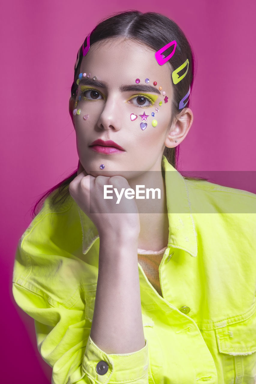 Studio portrait of a young girl in neon jacket on pink background with inspired make up