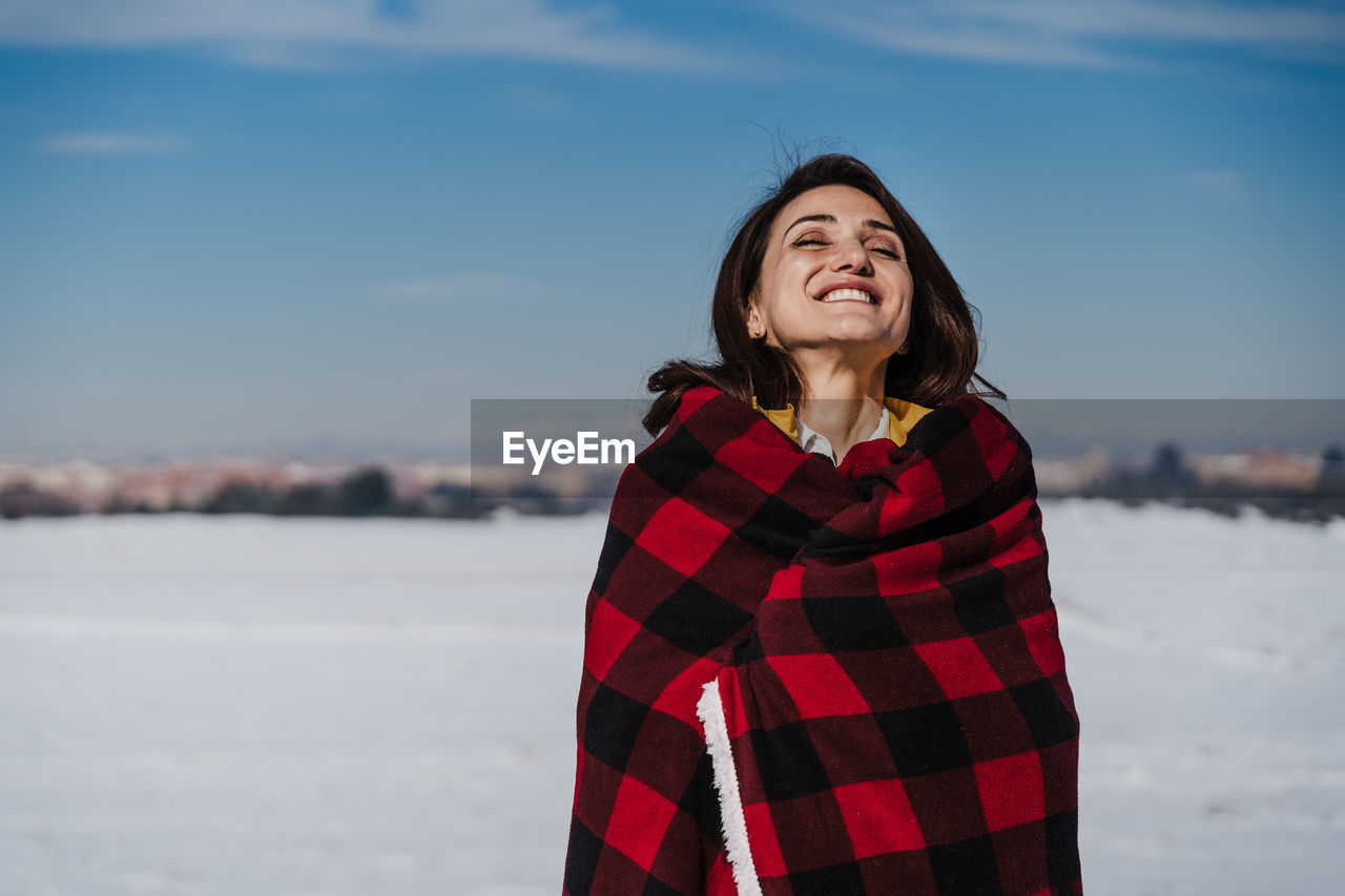 Smiling young woman standing in snow against sky