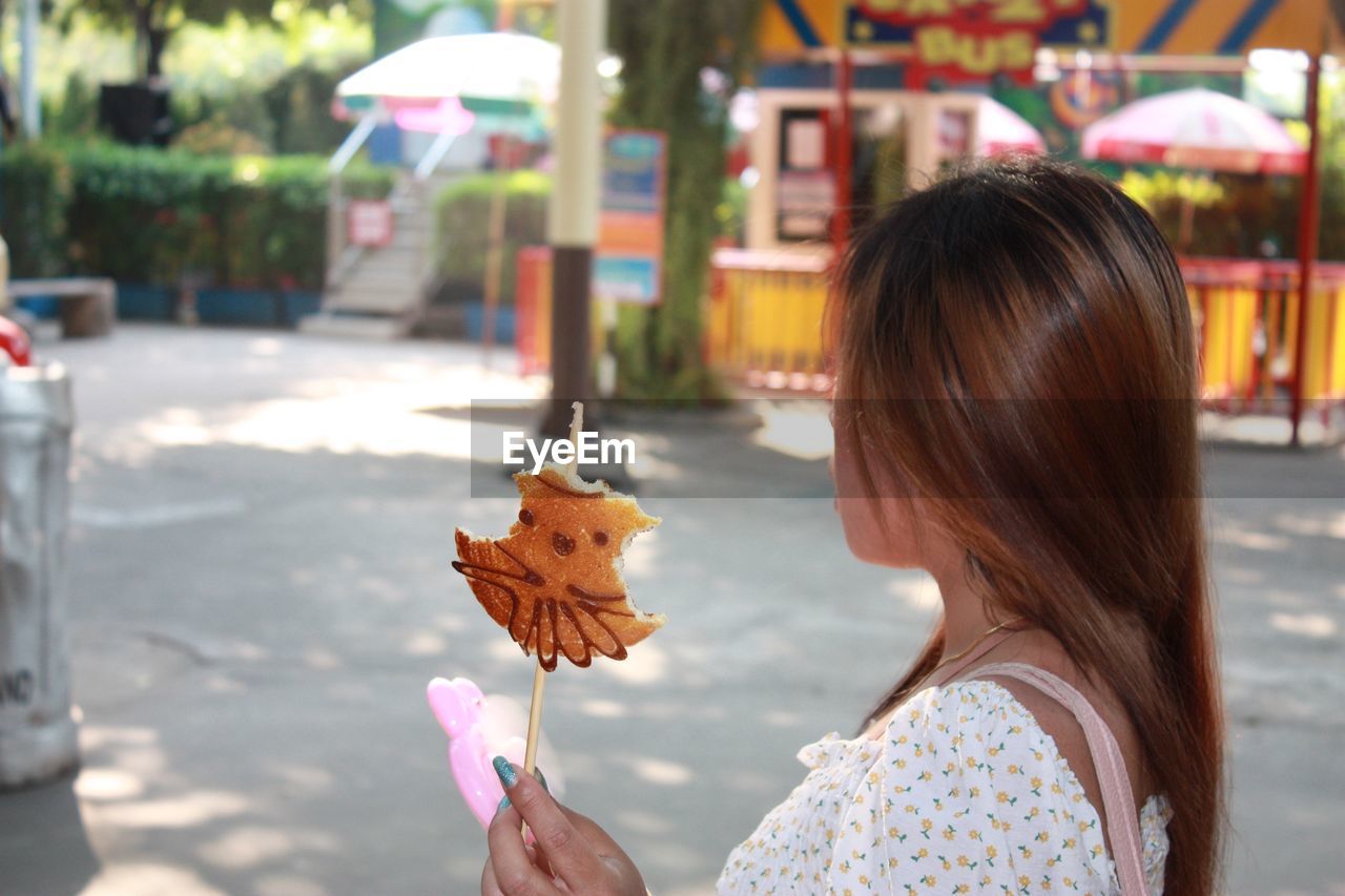 Side view of woman having food while standing in city