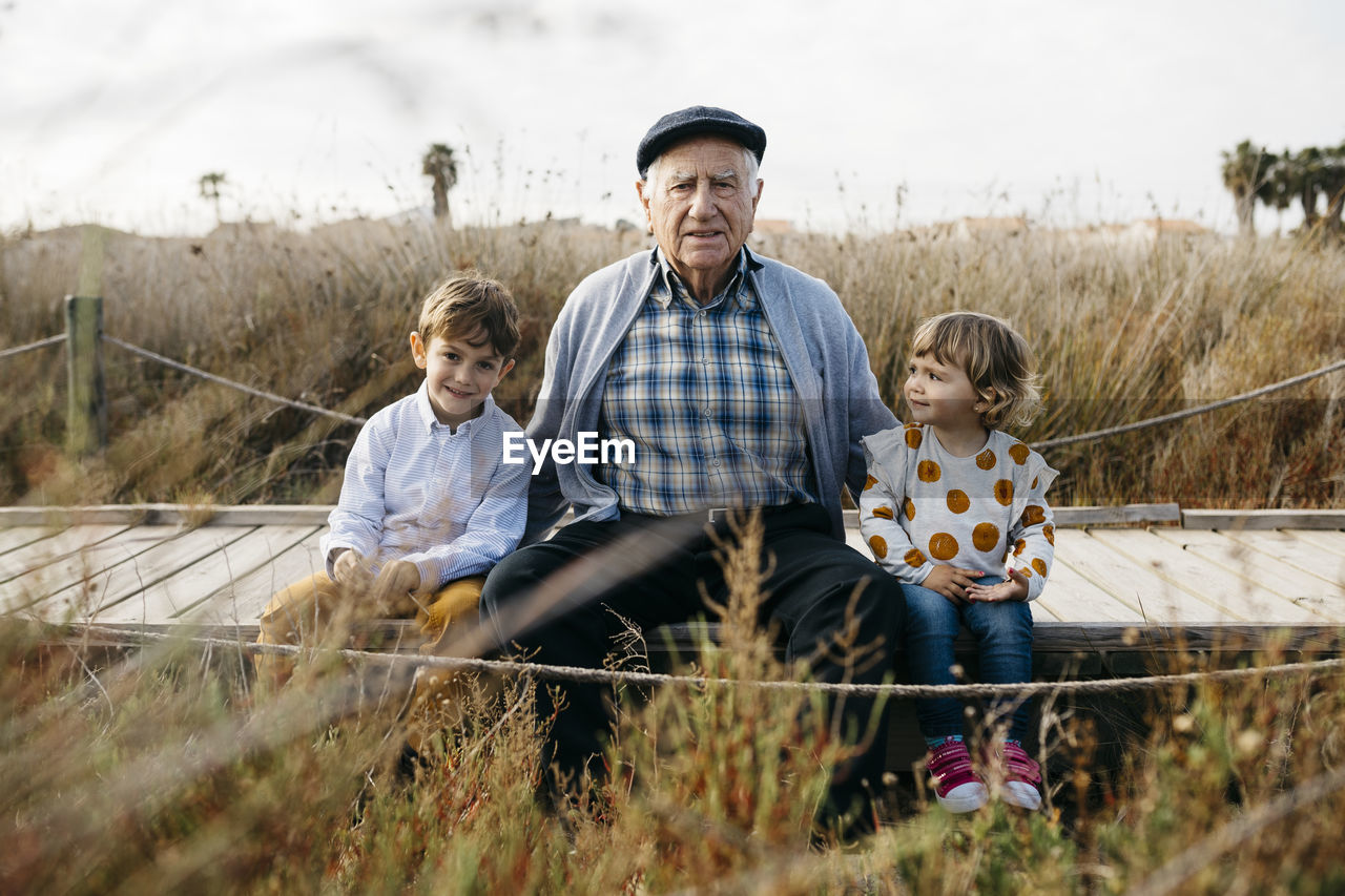 Portrait of grandfather sitting with his grandchildren side by side on boardwalk